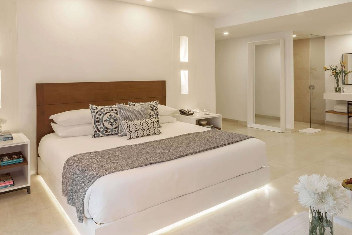 Een moderne hotelkamer met een groot bed, nachtkastjes, een badkamer met spiegel en een vaas met bloemen.