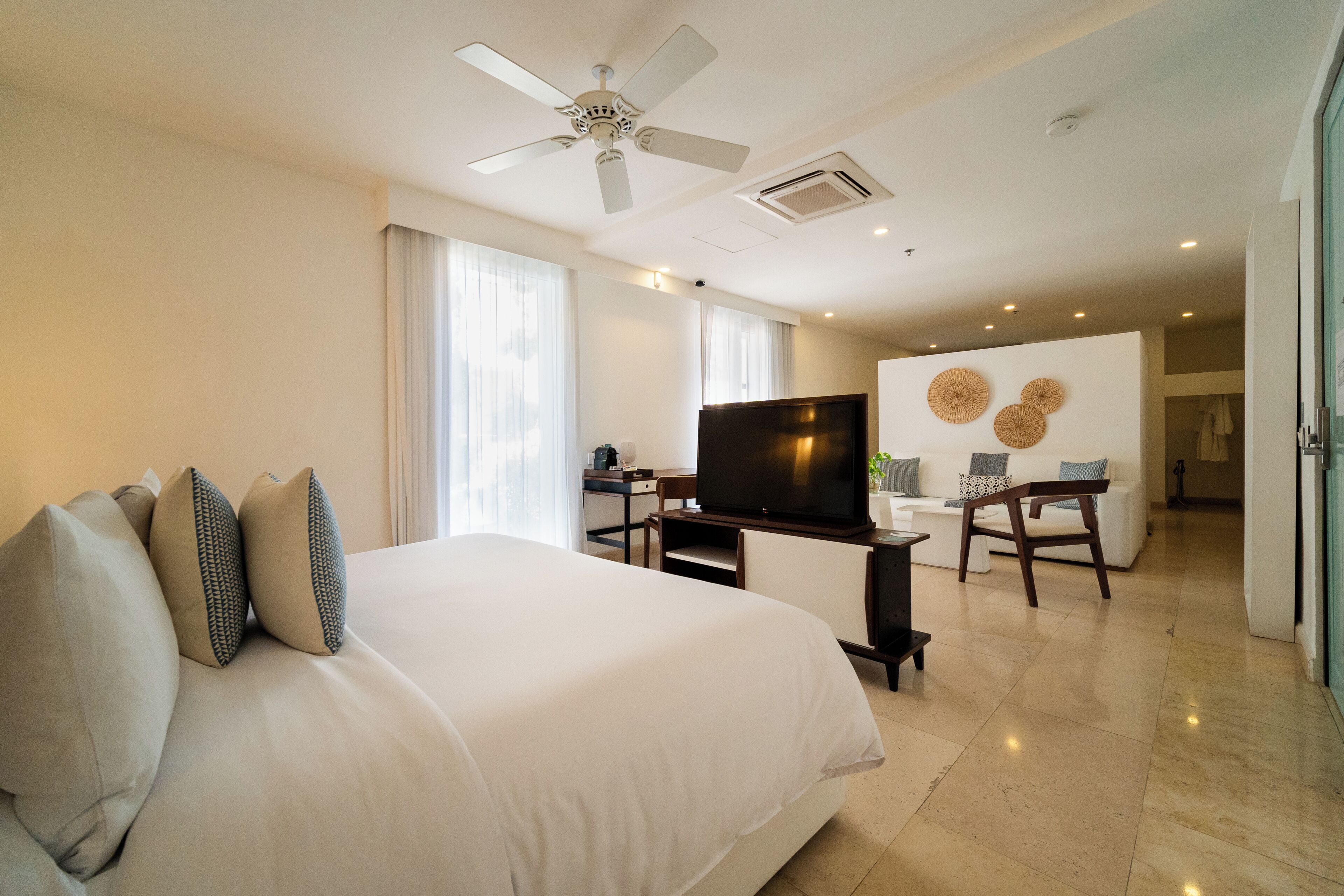 A hotel room with a large bed, a TV, a desk with a chair, and a dining area with a table and chairs.