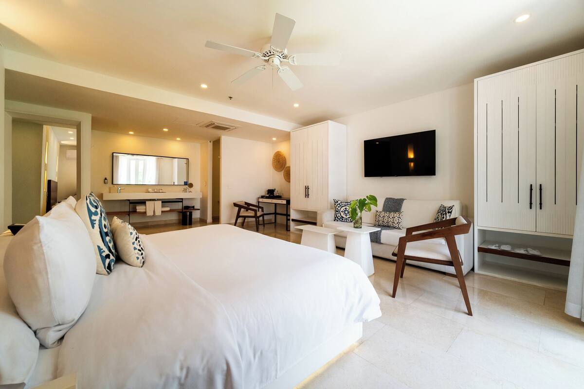 Un dormitorio moderno con una cama grande, un escritorio, un sofá y un televisor montado en la pared.