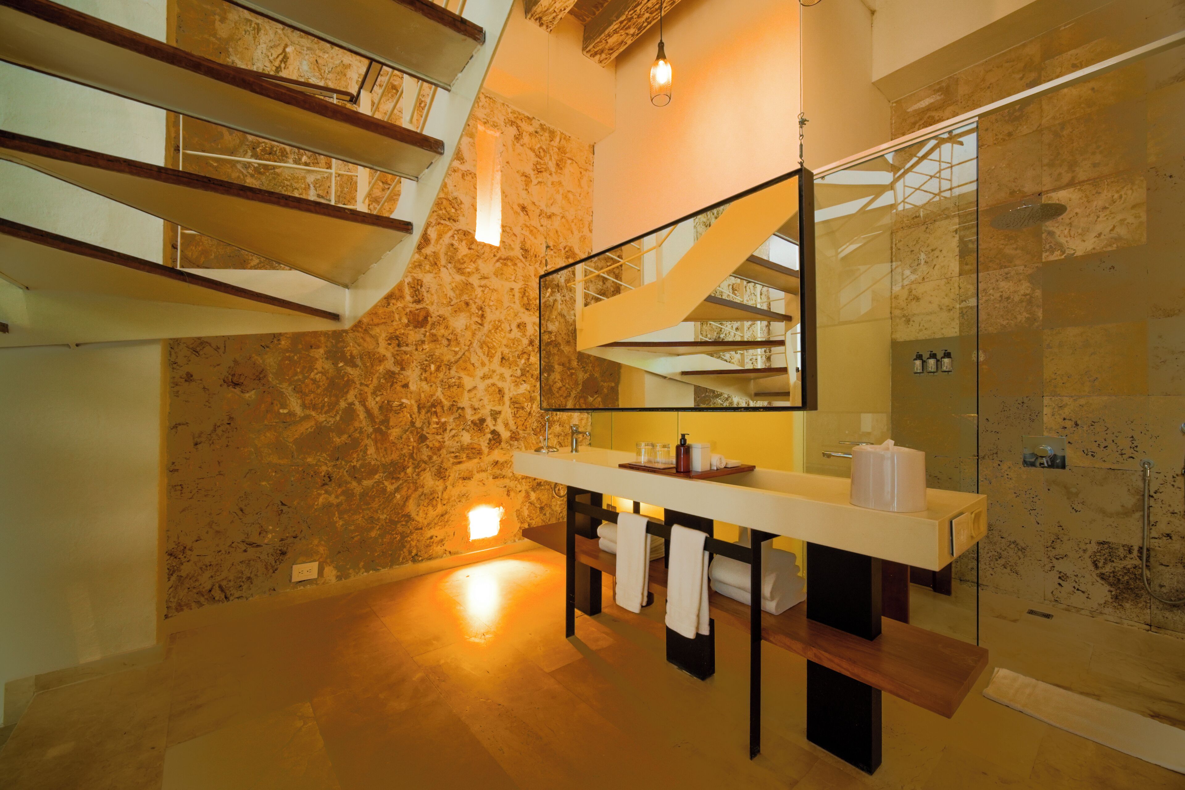 A modern bathroom with a stone wall, a large mirror, a sink, and a glass-enclosed shower.