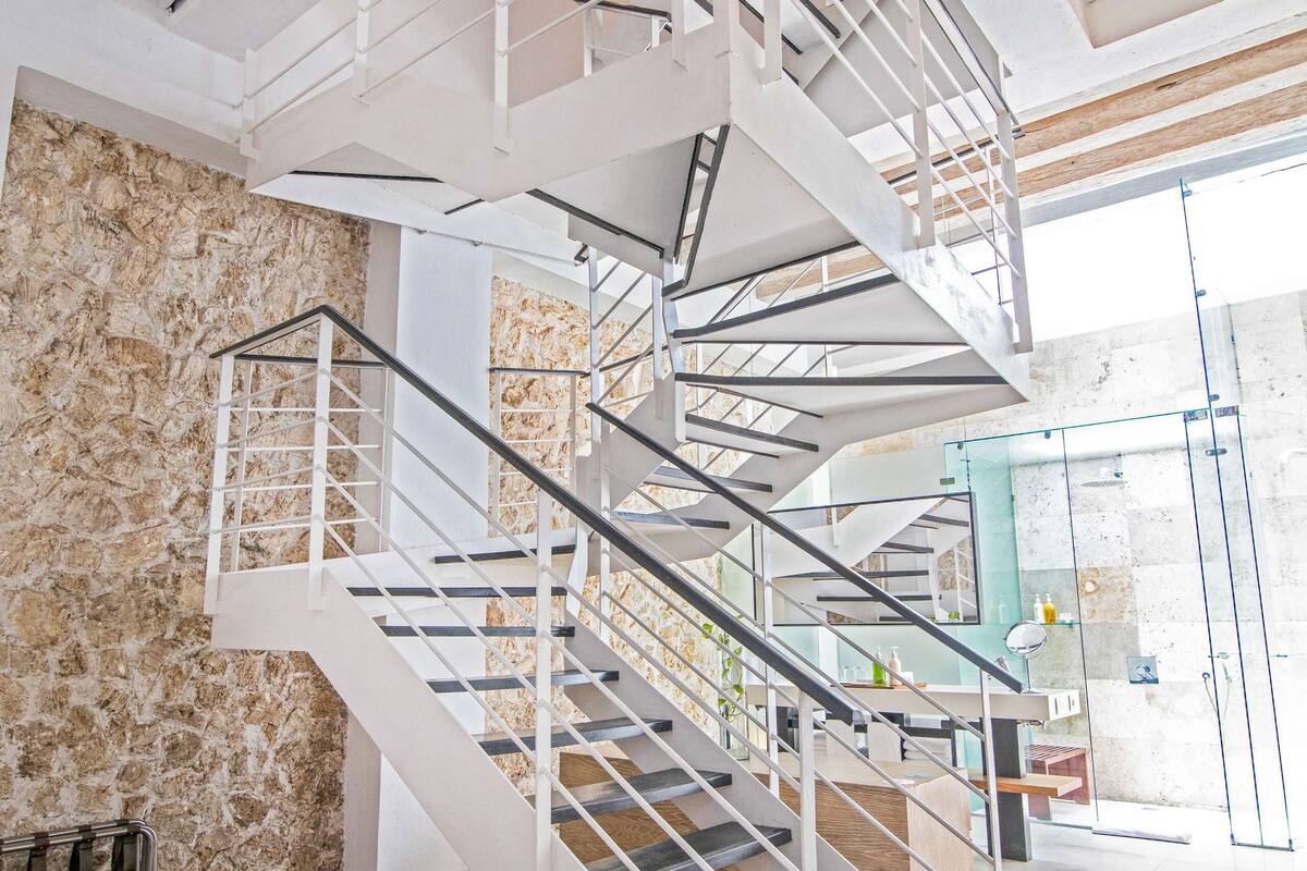 Un interior moderno con una escalera de caracol, pared de piedra y un ventanal grande.