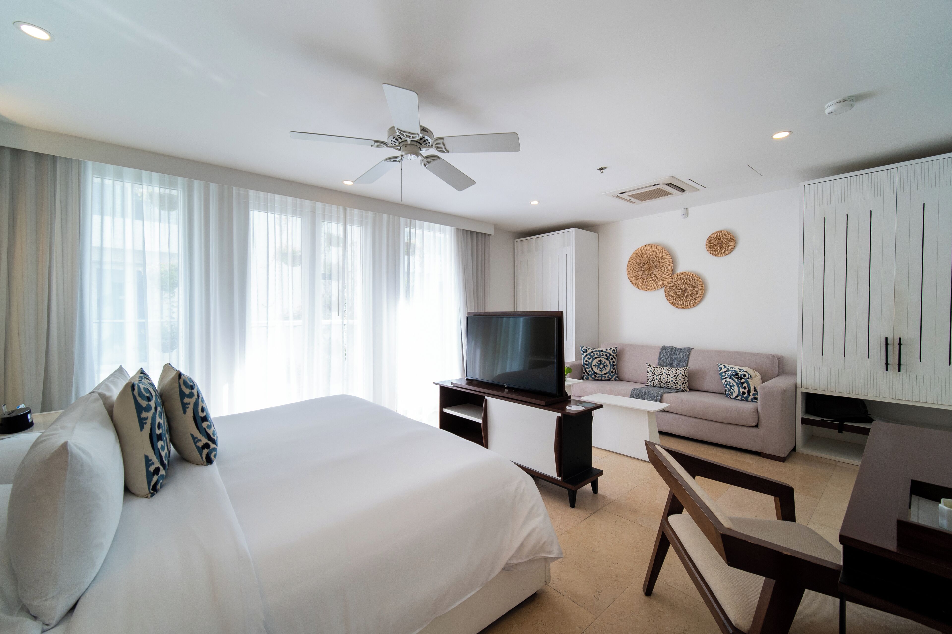 A modern hotel room with a large bed, a sofa, a TV, and a desk.