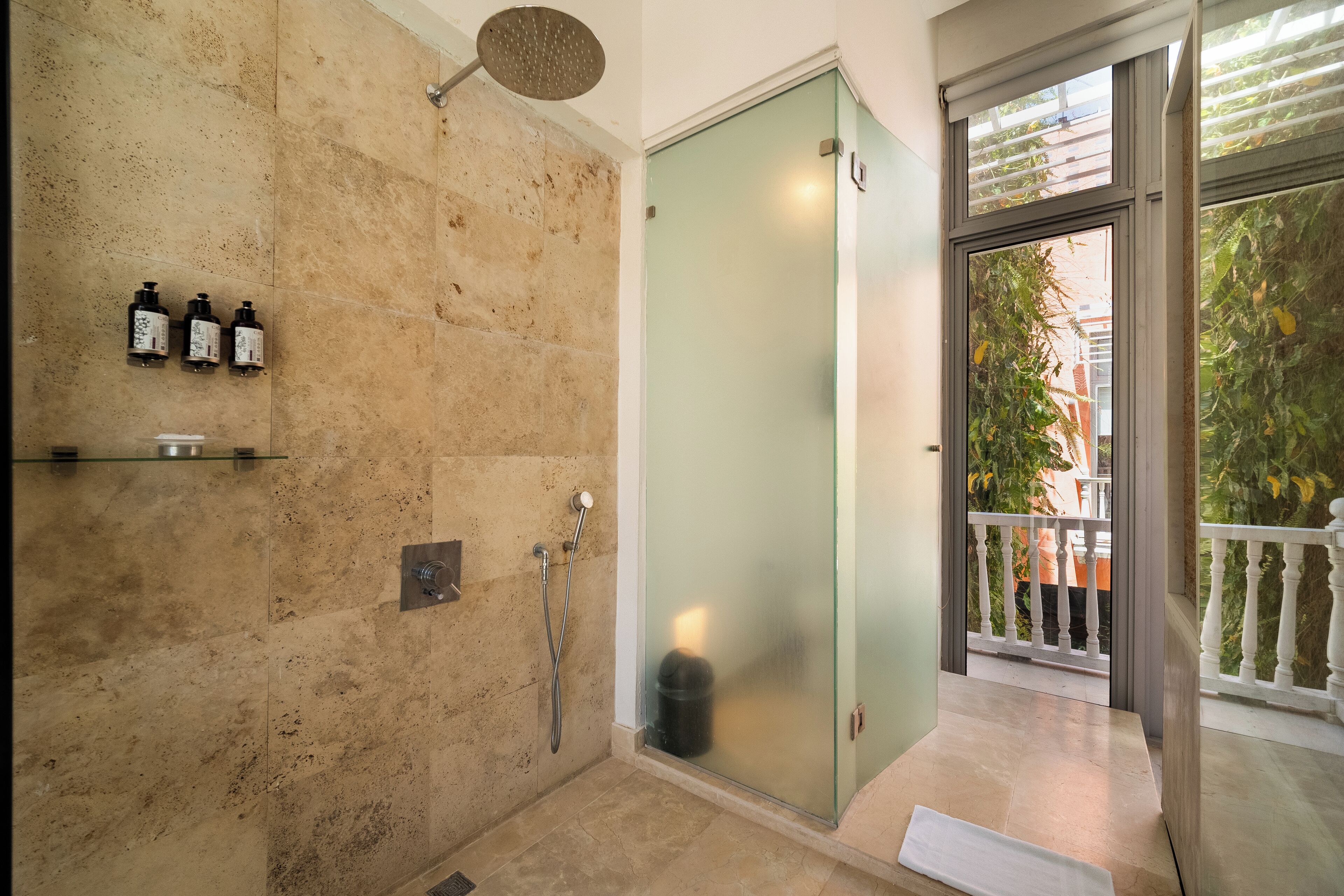 A modern bathroom with a glass shower enclosure, a beige tiled wall, and a small shelf with toiletries.