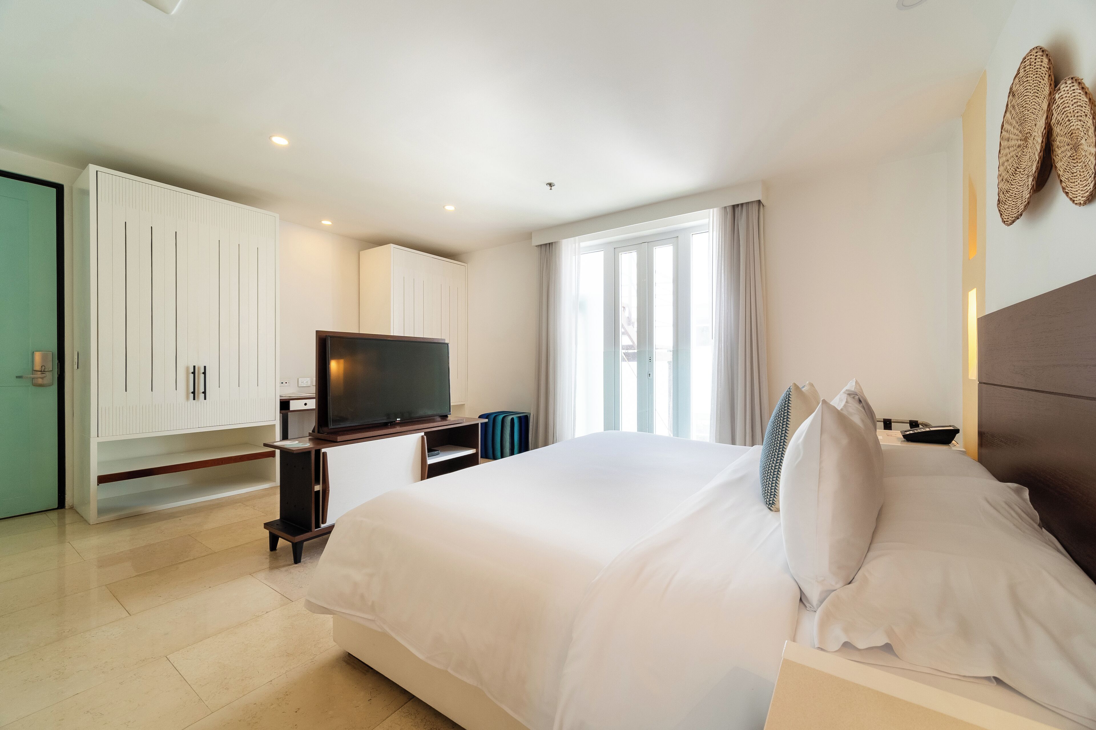 Quarto de hotel moderno com uma cama grande, uma TV, um guarda-roupa e uma janela com cortinas.