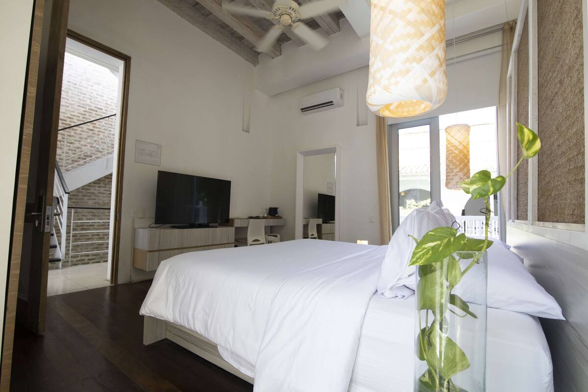Un dormitorio moderno con una cama grande, un televisor, un escritorio y una escalera que lleva a un área exterior.