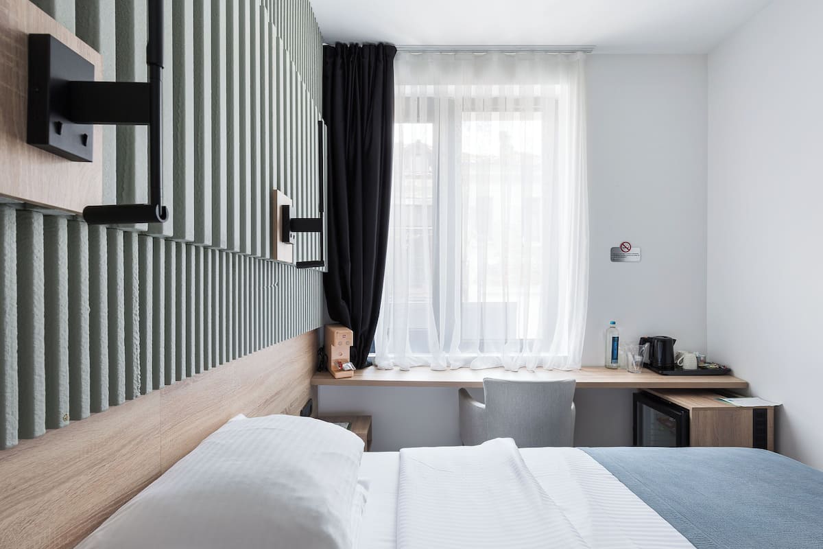 Ein Hotelzimmer mit Bett, Schreibtisch und einem Fenster mit durchsichtigen Vorhängen.
