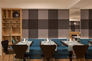 A restaurant with booths and tables, wooden shelves with books and a clock, and a checkered wall.