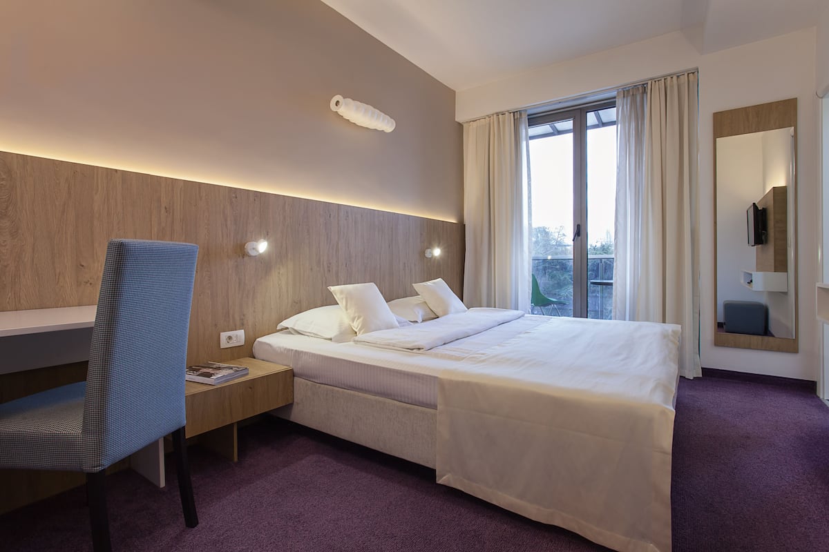 Ein Hotelzimmer mit Bett, Schreibtisch, Stuhl, Spiegel und einem Fenster mit Vorhängen.