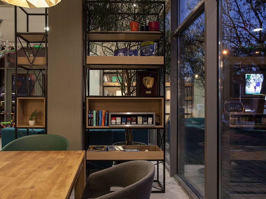 A modern interior with a wooden table, chairs, a bookshelf, and a large window.