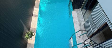 Una piscina en la azotea con superficie de agua azul cristalina, rodeada por una terraza de madera y barandales metálicos.