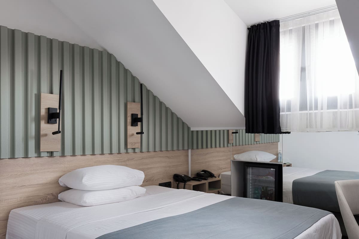 Ein Hotelzimmer mit Bett, Nachttisch, Lampe und einem großen Fenster mit Vorhängen.