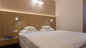 Een hotelkamer met een houten hoofdbord, twee witte kussens, een opgemaakt bed en een tijdschrift op het nachtkastje.