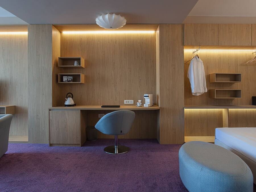 Une chambre d’hôtel moderne avec un bureau en bois, une chaise, un lit et un téléviseur.