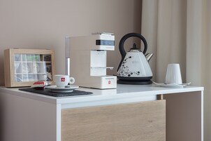 A modern kitchenette with a coffee maker, tea kettle, and a framed picture on the counter.