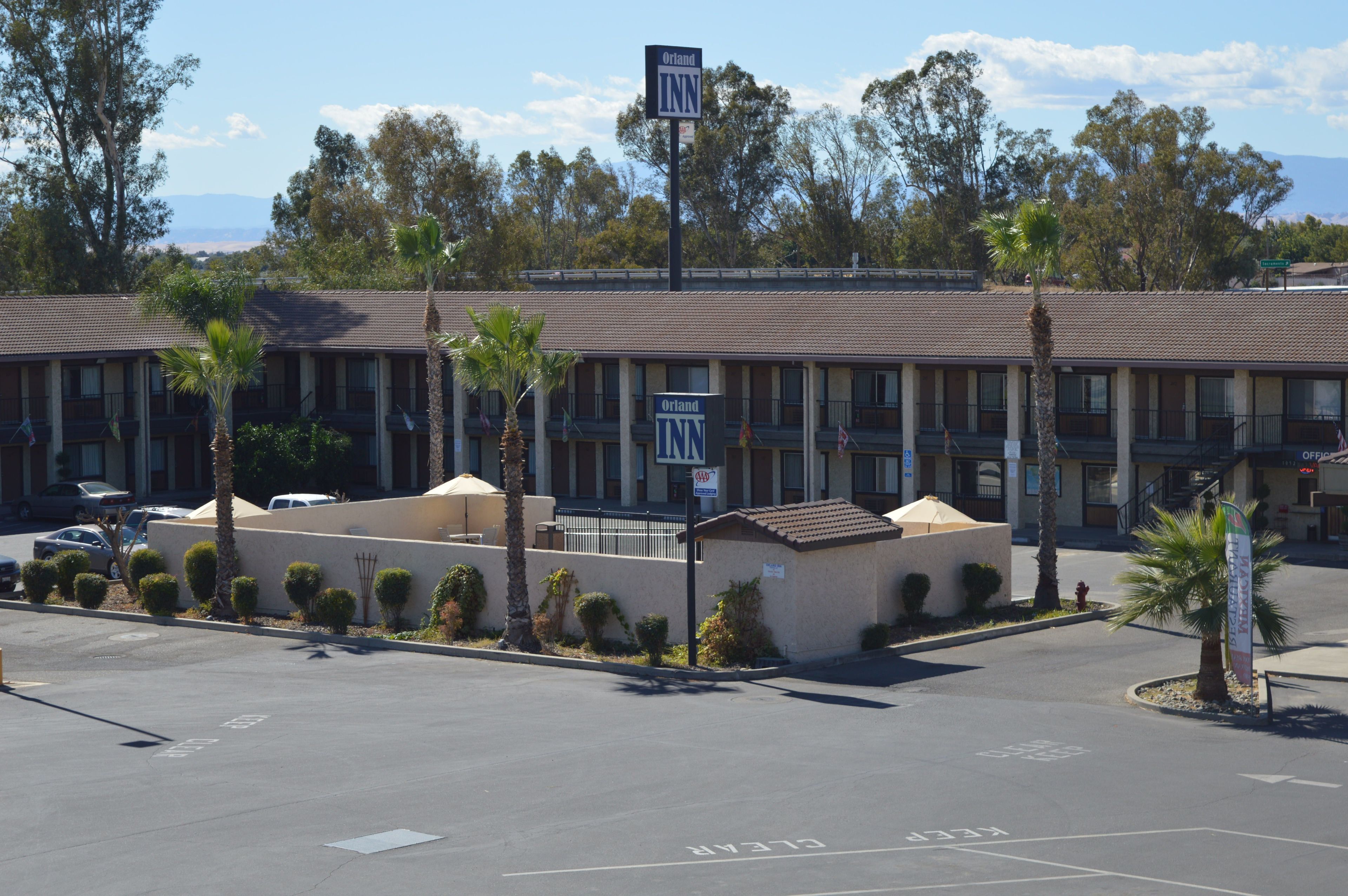 A motel with a signboard, parking lot, and surrounding trees.