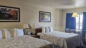 A hotel room with two beds, a desk, a chair, and two paintings on the wall.