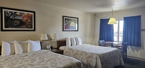 A hotel room with two beds, a desk, a chair, and two paintings on the wall.