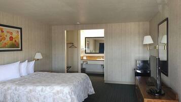 Habitación de hotel con una cama, un escritorio con computadora, un espejo y un cuadro en la pared.