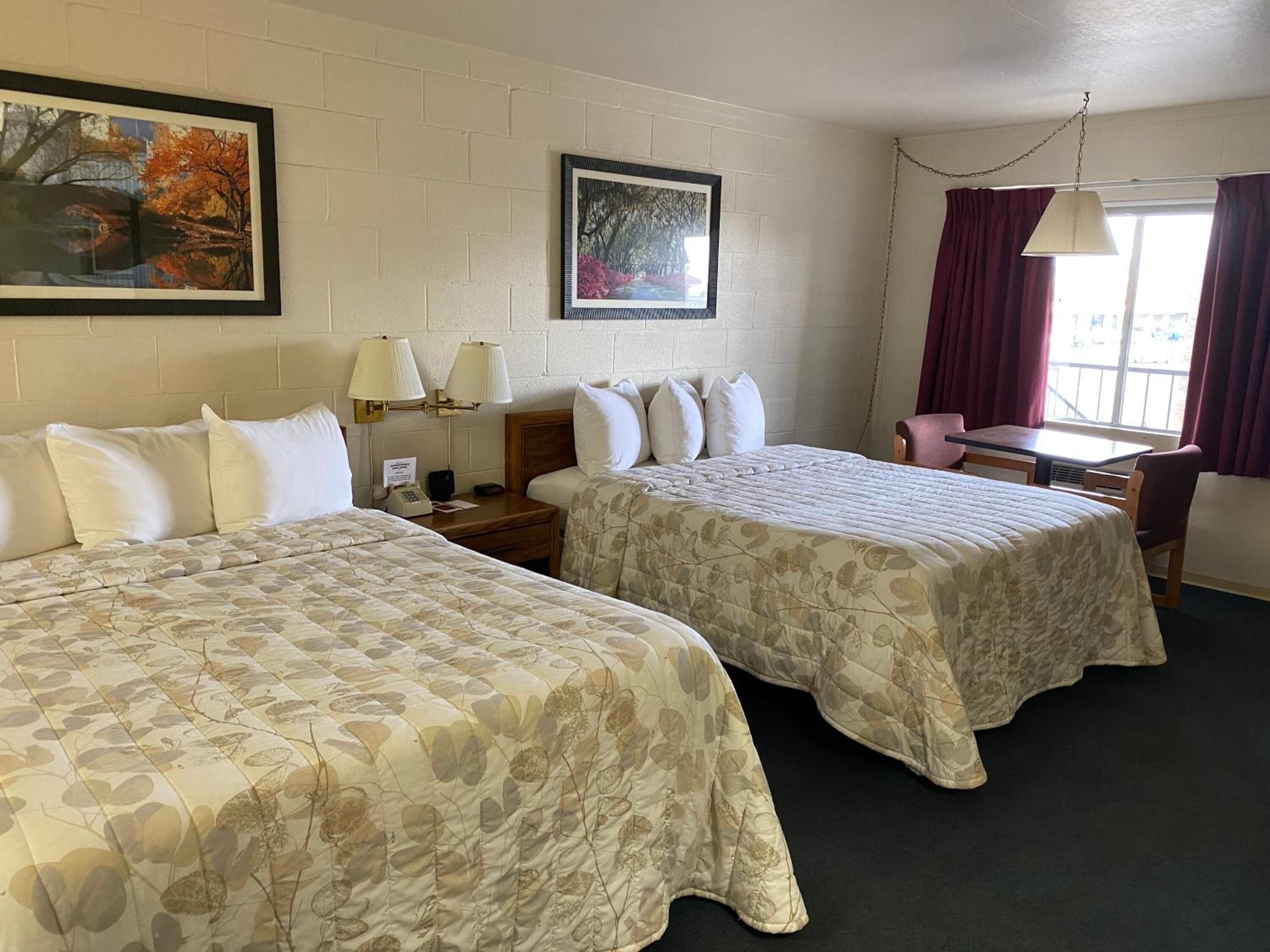 Habitación de hotel con dos camas, un escritorio, una silla y dos lámparas.