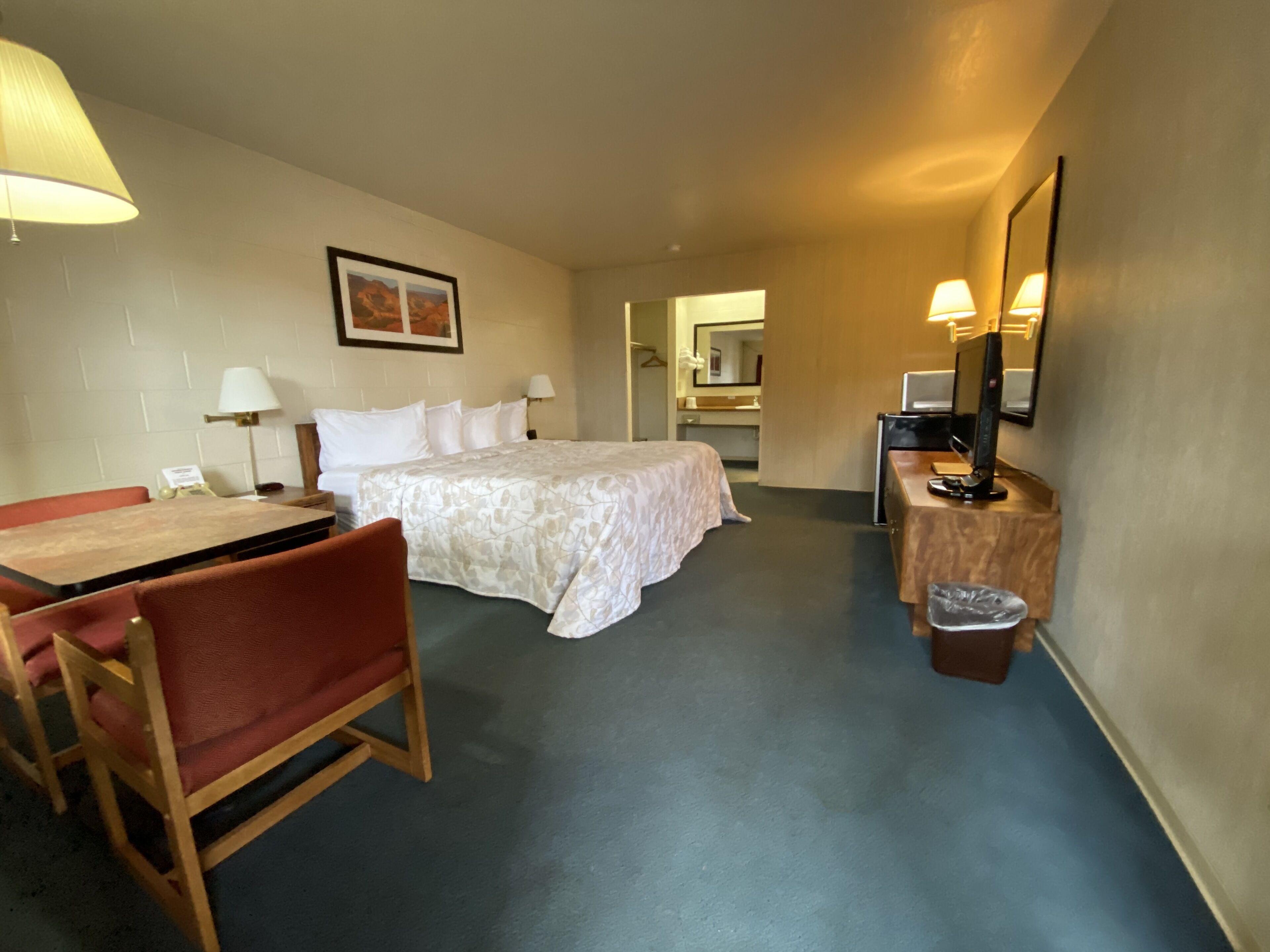 Habitación de hotel con cama, escritorio con silla, mesita pequeña, cubo de basura y espejo.