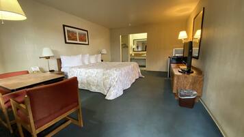 Habitación de hotel con cama, escritorio con silla, mesita pequeña, cubo de basura y espejo.