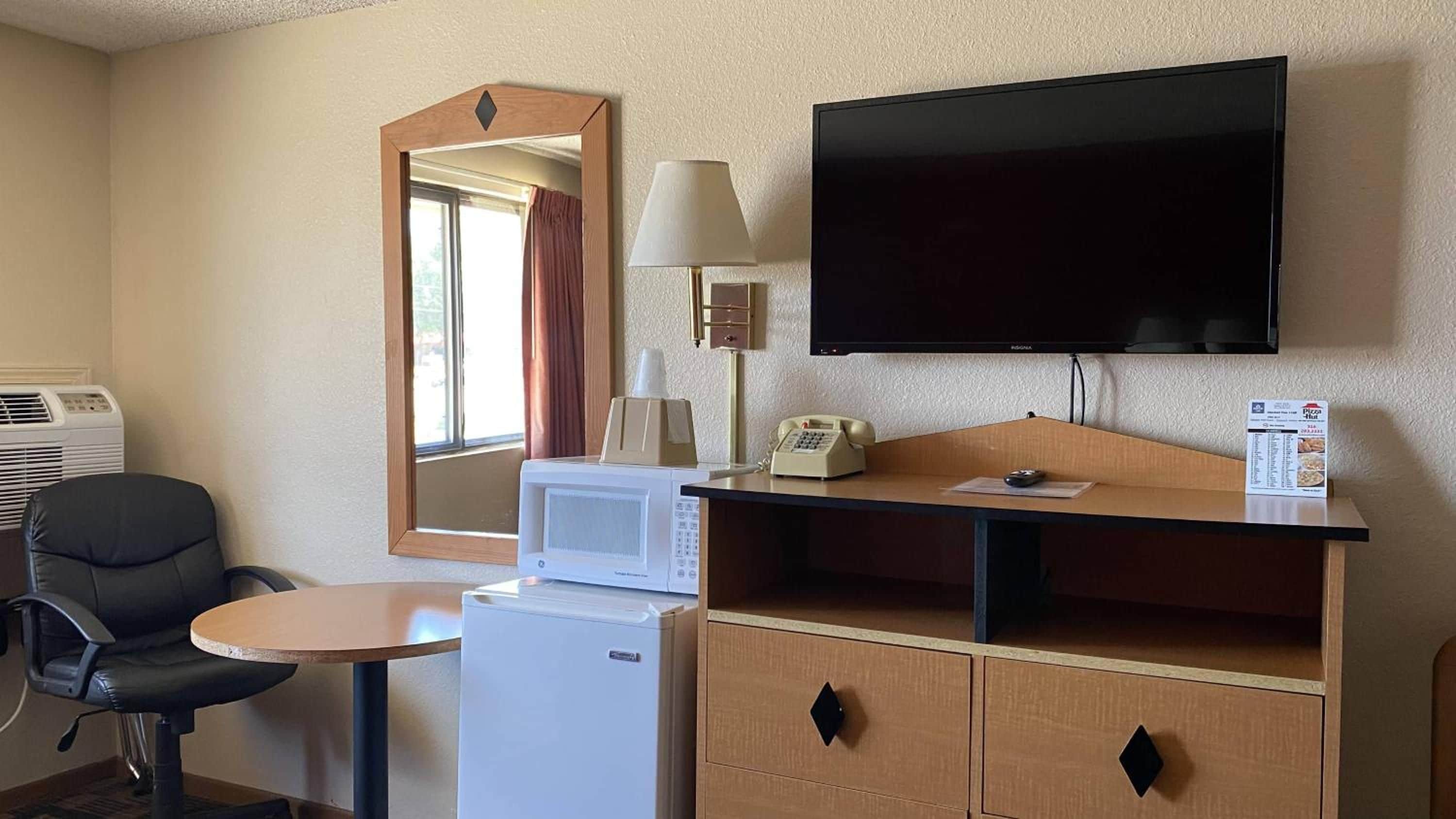 Une chambre d’hôtel équipée d’un bureau, d’une chaise, d’un four à micro-ondes, d’un réfrigérateur, d’une télévision et d’un miroir.