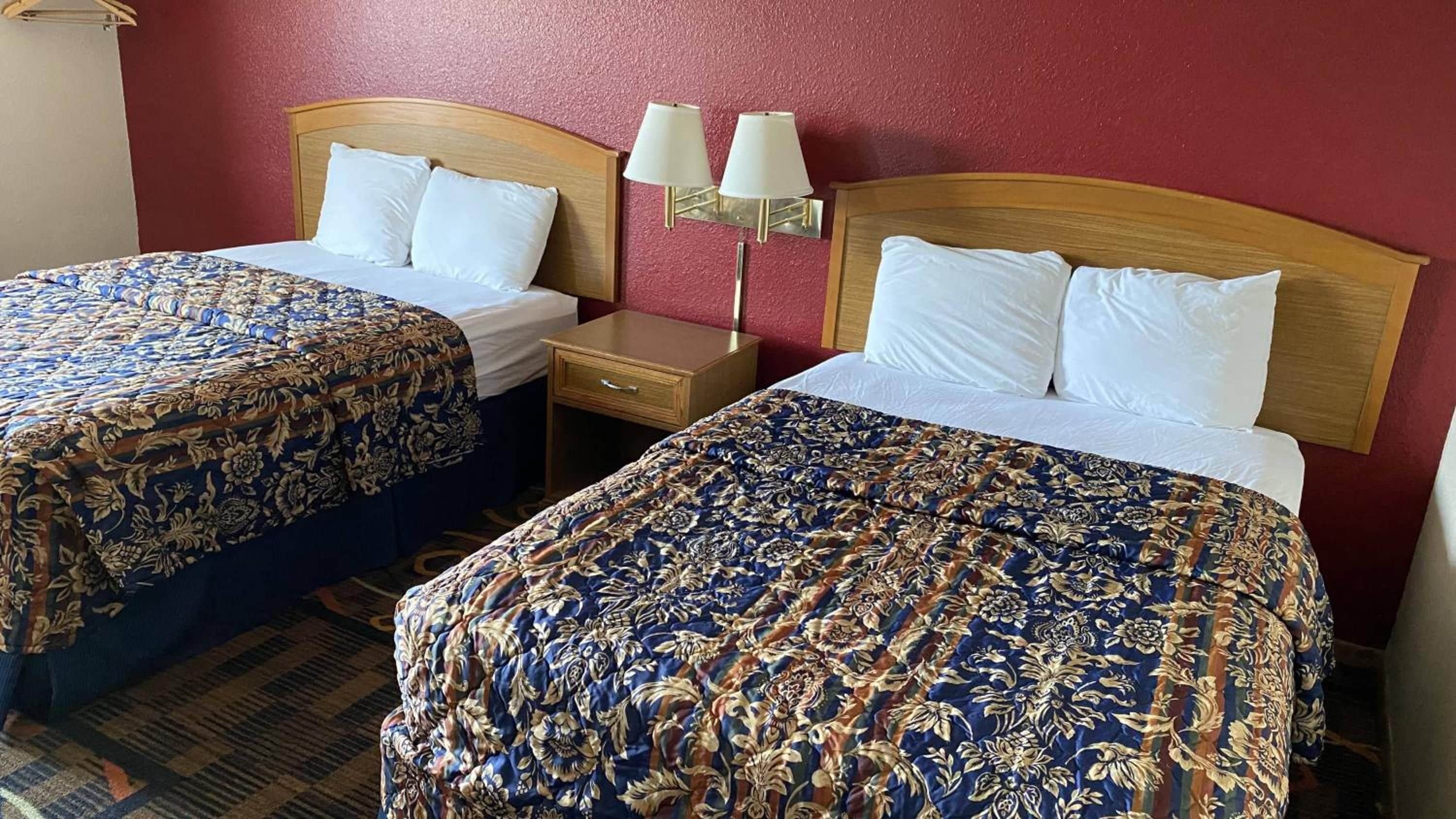 Una habitación de hotel con dos camas, cada una con cubrecama estampado con motivos florales, un cabecero de madera y una mesita de noche con lámpara.