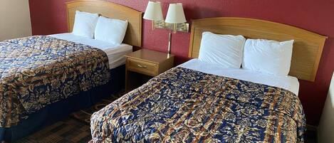 A hotel room with two beds, each with a floral-patterned bedspread, a wooden headboard, and a nightstand with a lamp.