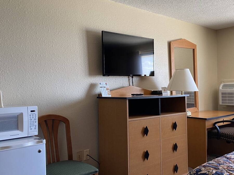A hotel room with a bed, a desk with a lamp, a television, a microwave, and an air conditioner.