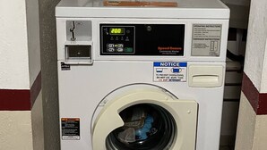 Une laveuse commerciale à chargement frontal dotée d’un écran numérique, d’un manuel d’utilisation et d’une étiquette d’avertissement.