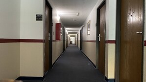 Un long couloir étroit, typique des hôtels, avec des portes des deux côtés, un sol recouvert de moquette et un panneau indiquant une zone non-fumeurs.