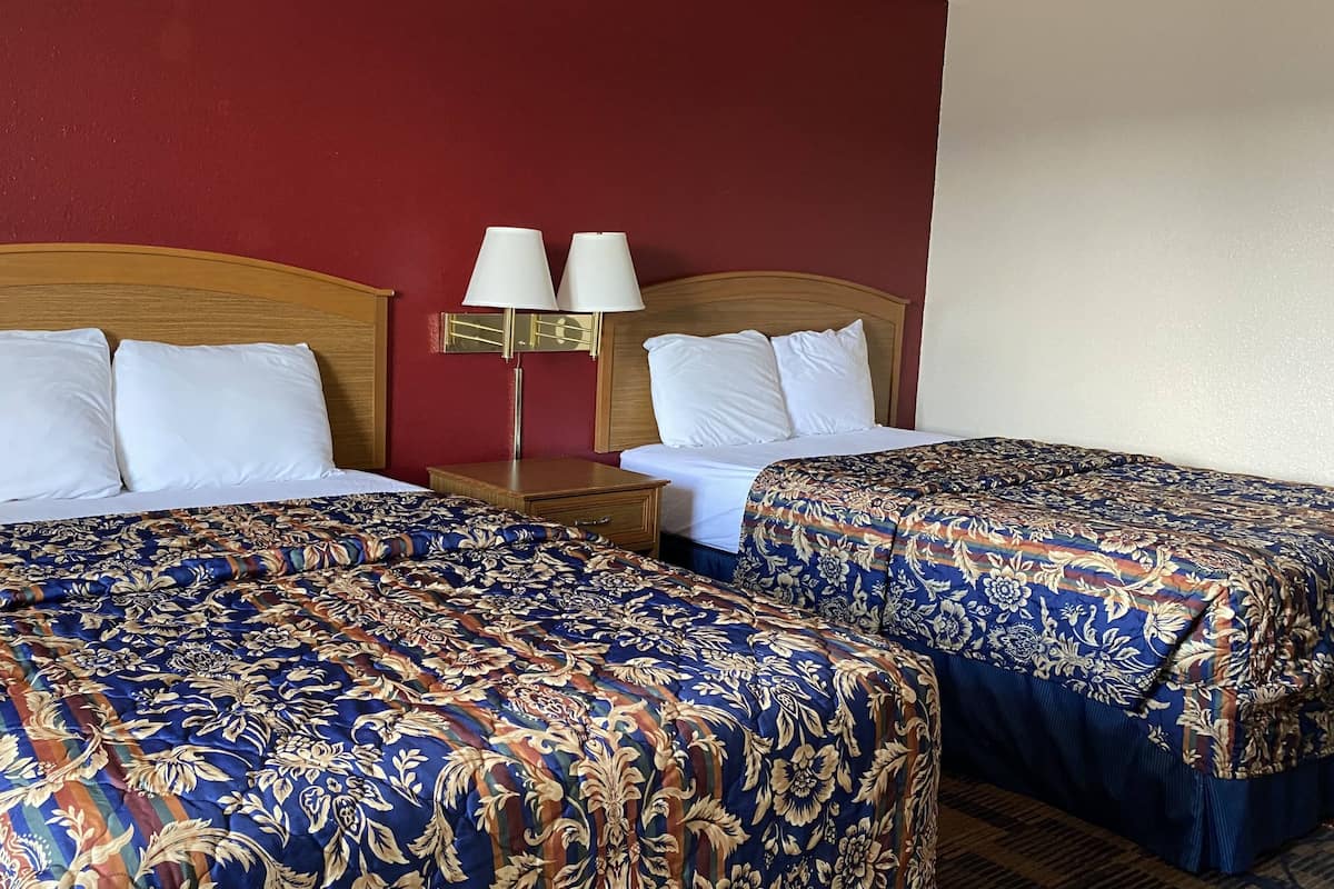 Habitación de hotel con dos camas, cada una con cubrecama estampado con motivos florales, cabecero de madera y mesita de noche con lámpara.