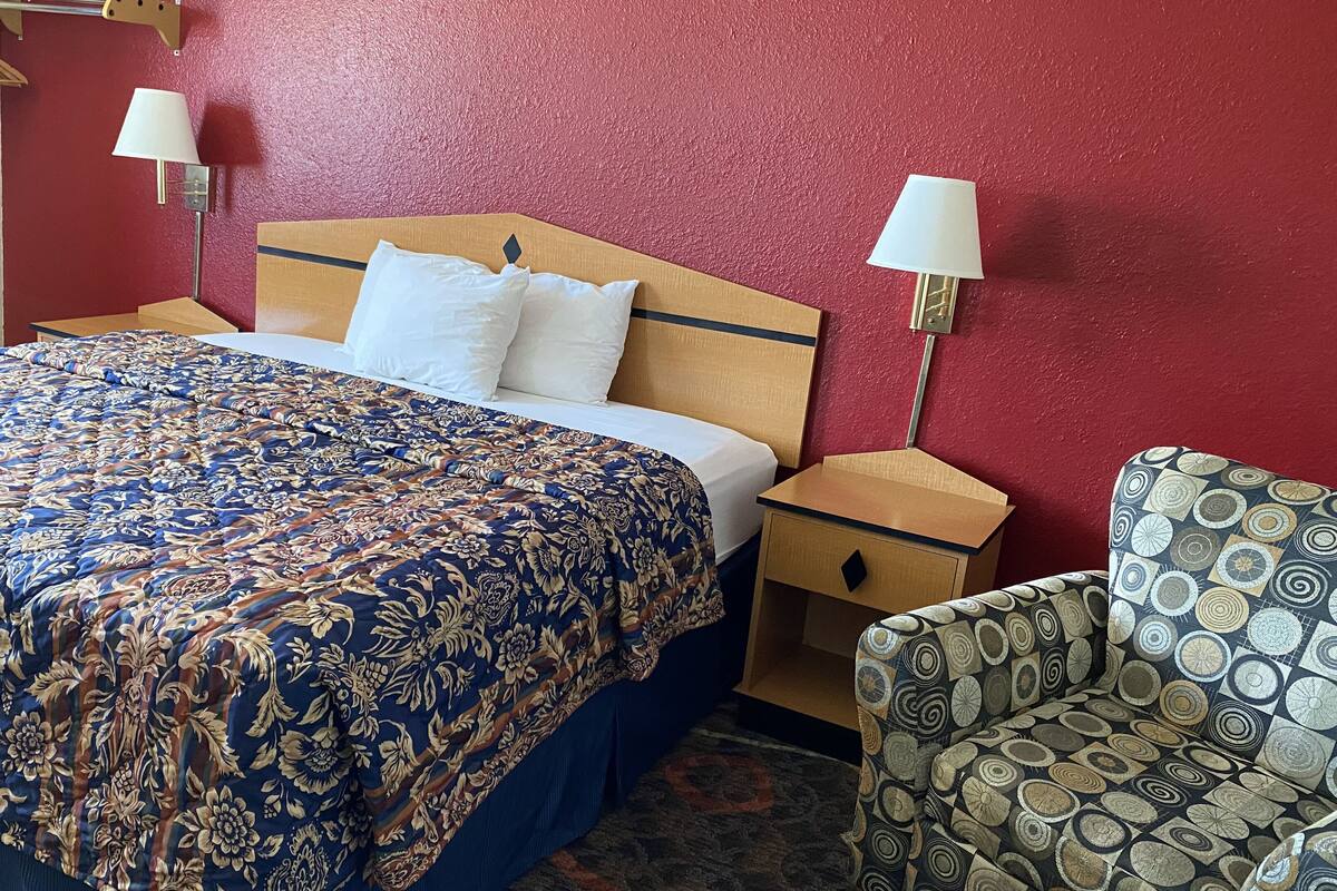 Una habitación de hotel con una cama grande, dos mesitas de noche, una silla y una pared roja.