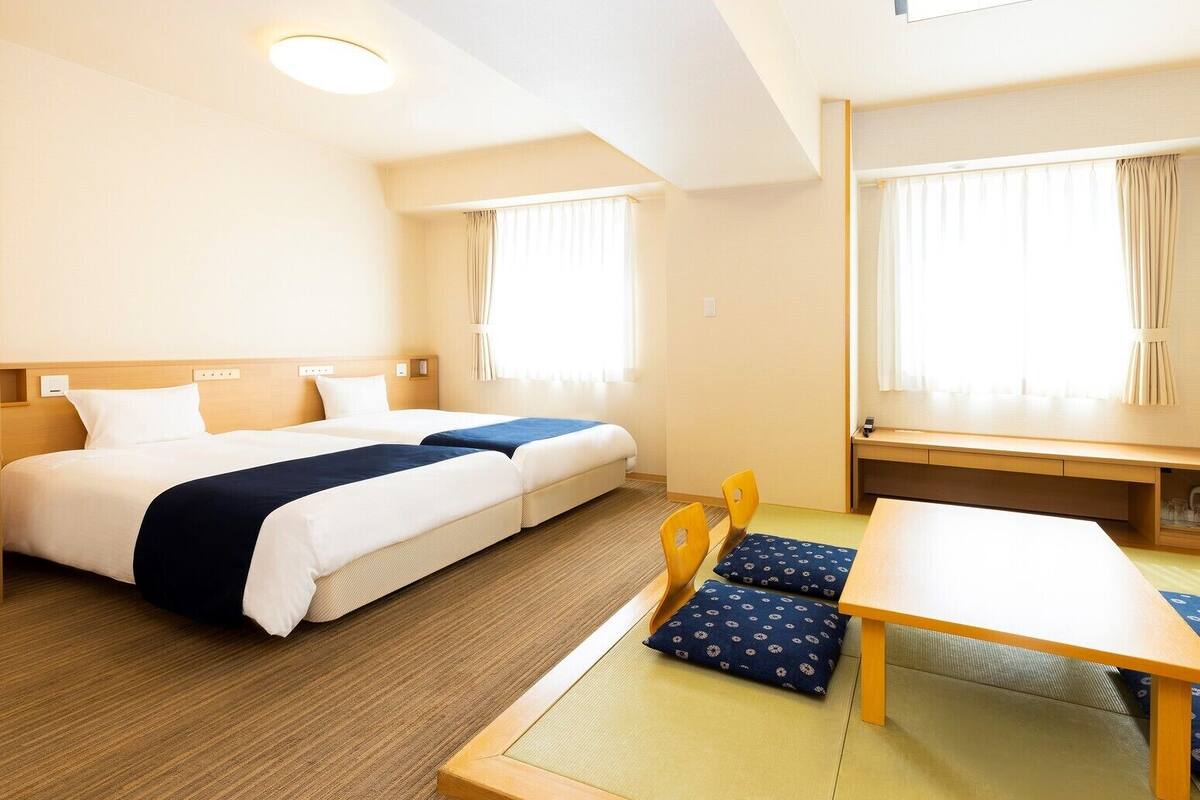 Une chambre d’hôtel avec deux lits, une table à manger, des chaises et une petite table avec une chaise.