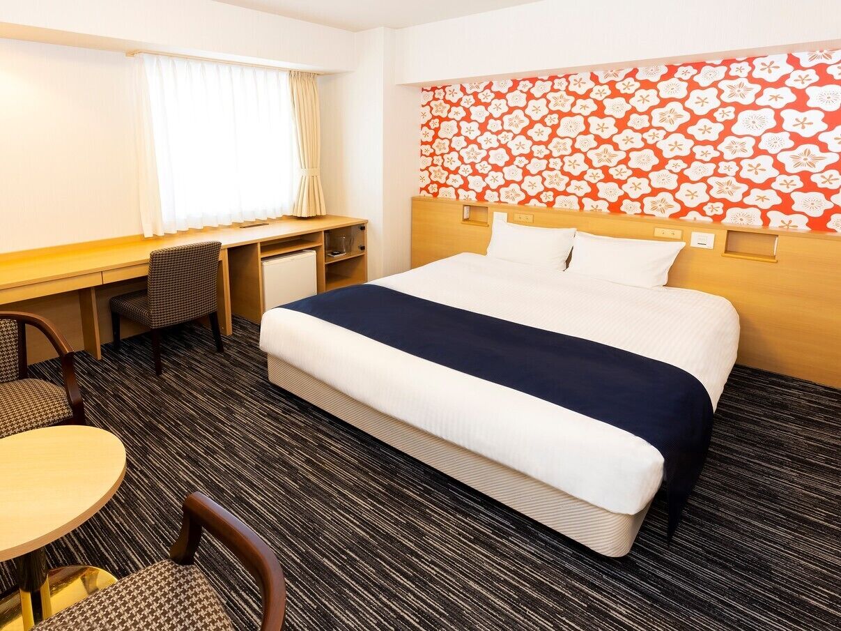 A hotel room with a bed, desk, chair, and a small table.