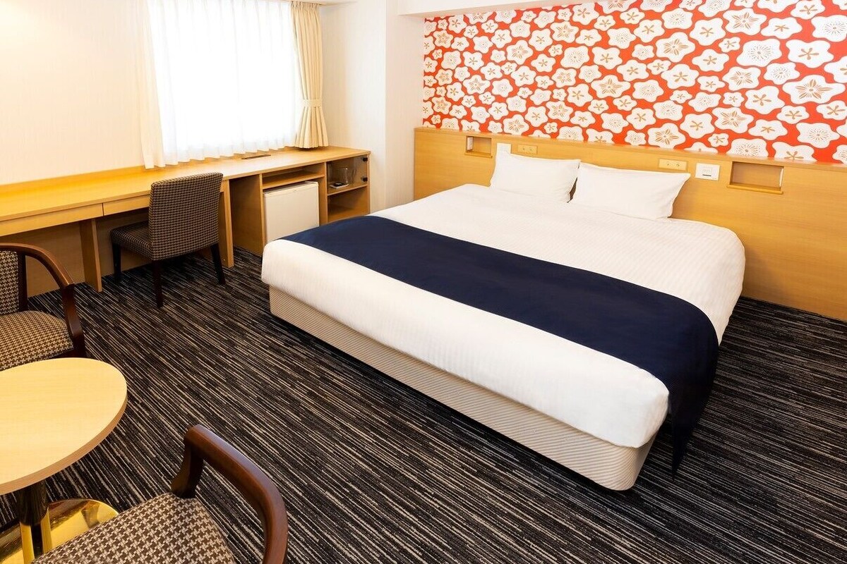 A hotel room with a bed, desk, chair, and a small table.
