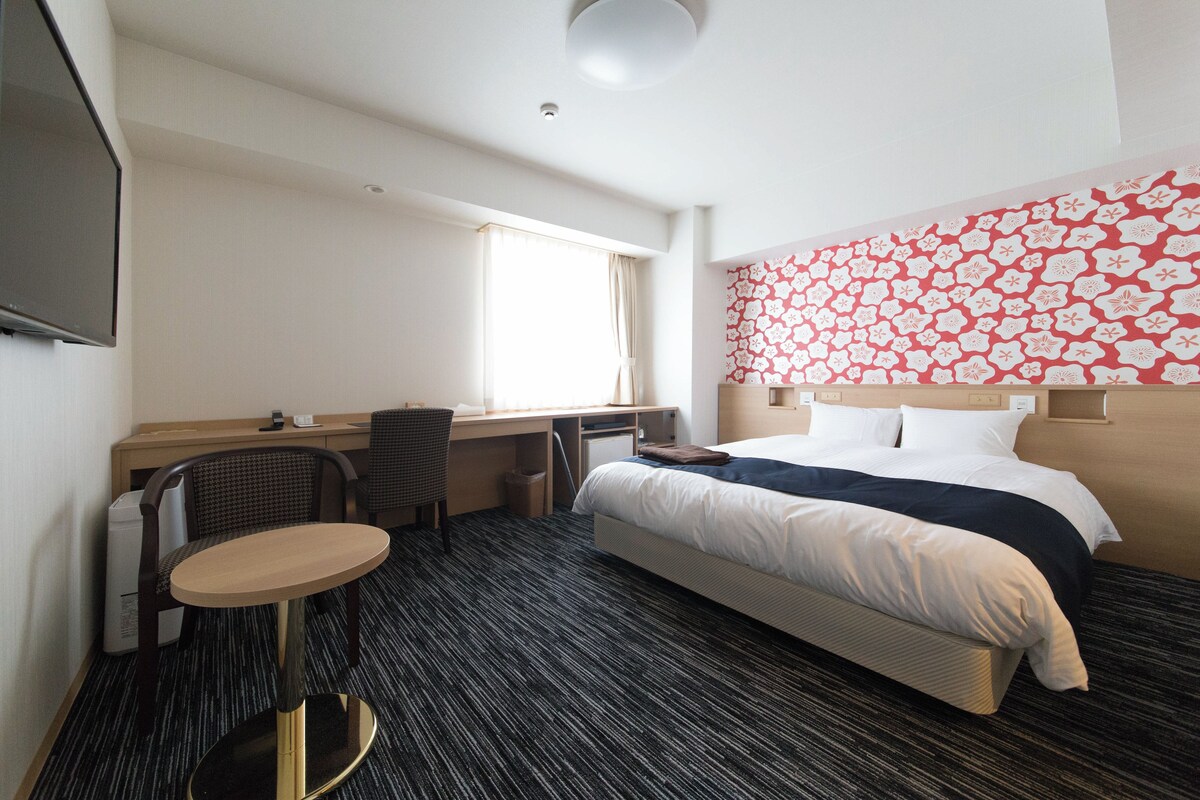 Una habitación de hotel con una cama, un escritorio, una silla y una pequeña mesa.