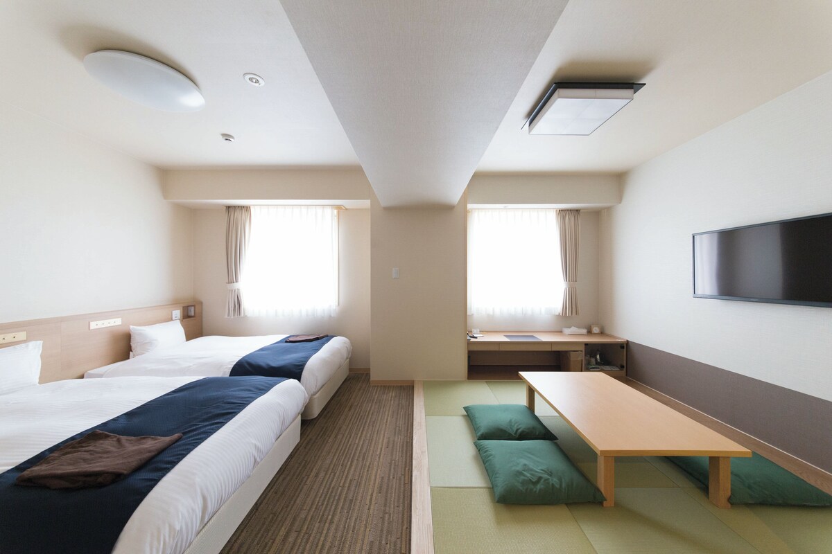 Habitación de hotel con dos camas, un escritorio, televisor y ventana.
