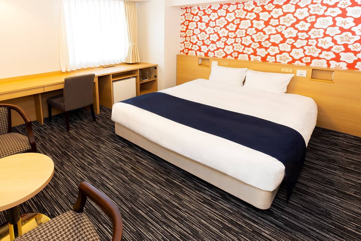 Une chambre d’hôtel avec un lit, un bureau, une chaise et une petite table.