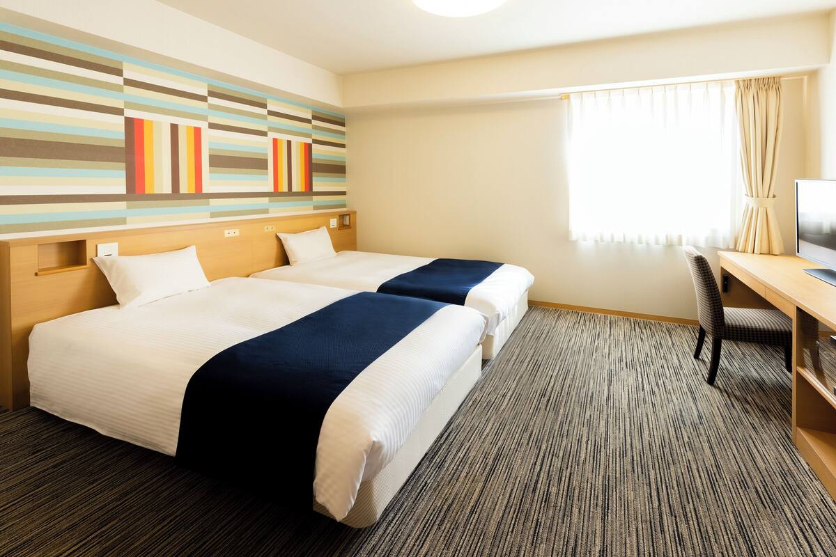 Une chambre d’hôtel avec deux lits, un bureau, une chaise et un téléviseur.