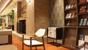 A lobby with a fireplace, seating area, and a bookshelf with books. - Hotel WBF Grande Asahikawa (Asahikawa)