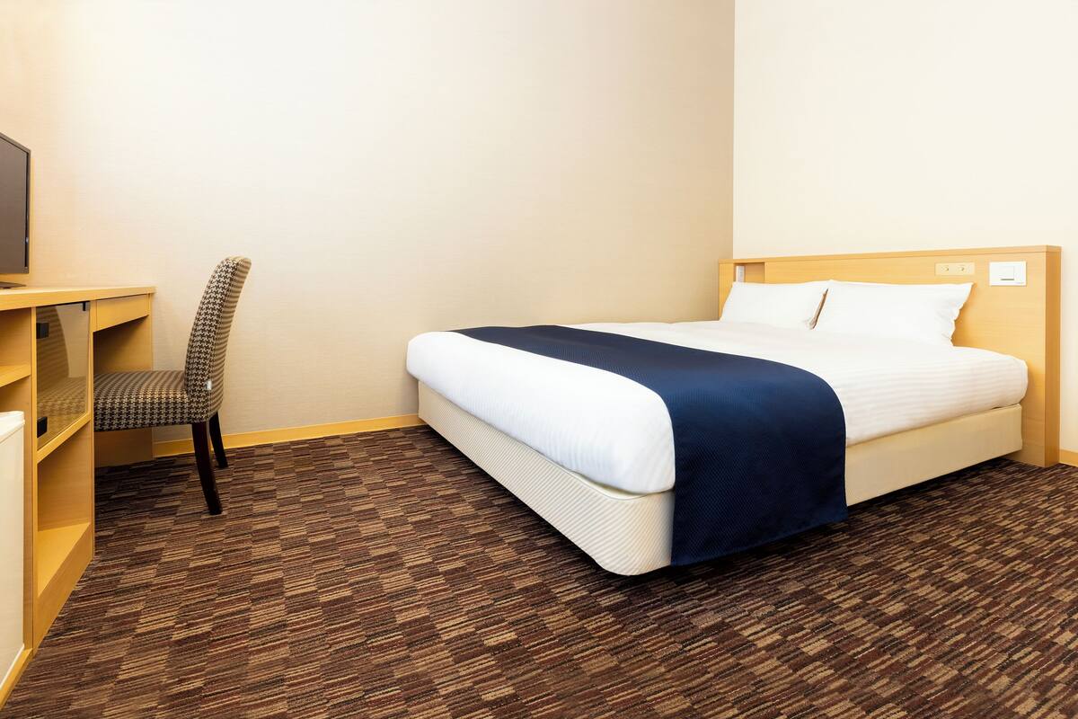 Une chambre d’hôtel avec un lit, un bureau, une chaise et un téléviseur.
