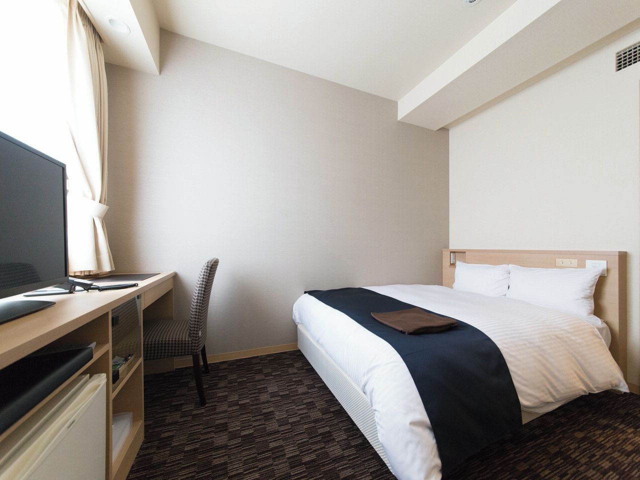 A hotel room with a bed, a desk, a chair, and a television.