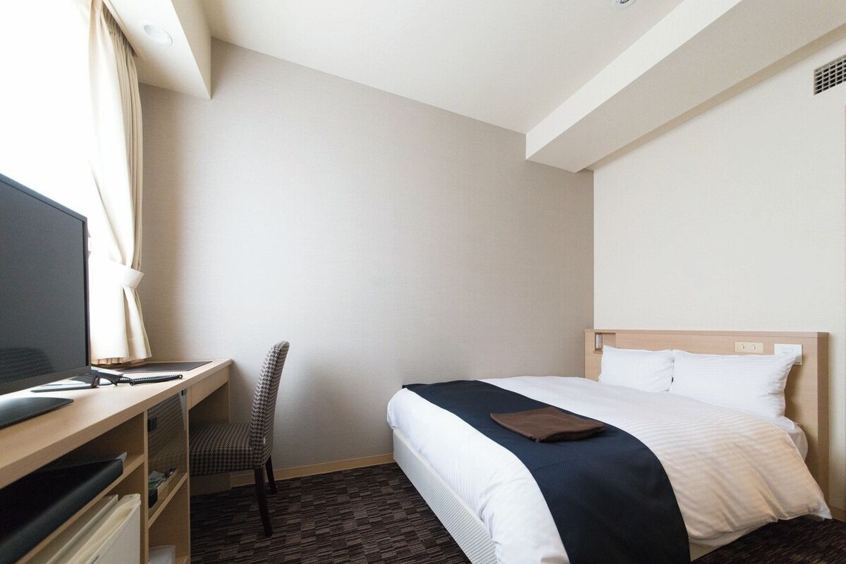 Una habitación de hotel con una cama, un escritorio, una silla y un televisor.
