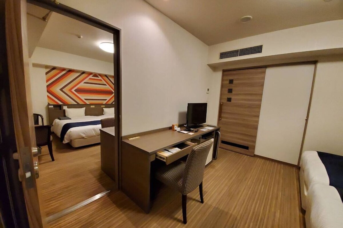 Una habitación de hotel con una cama, un escritorio con silla, un televisor y un armario.