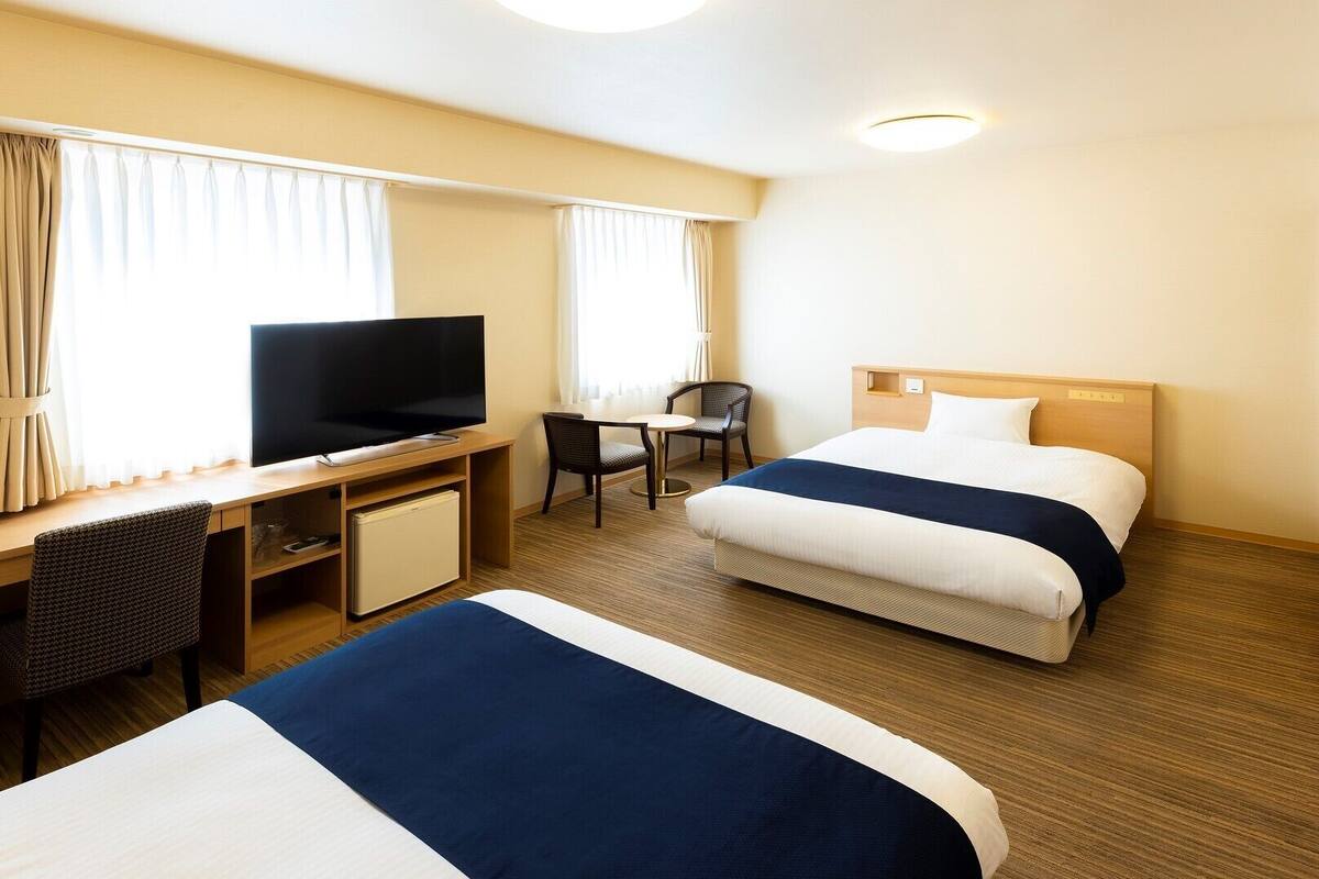 Une chambre d’hôtel avec deux lits, un bureau avec une télévision, une petite table et une chaise.