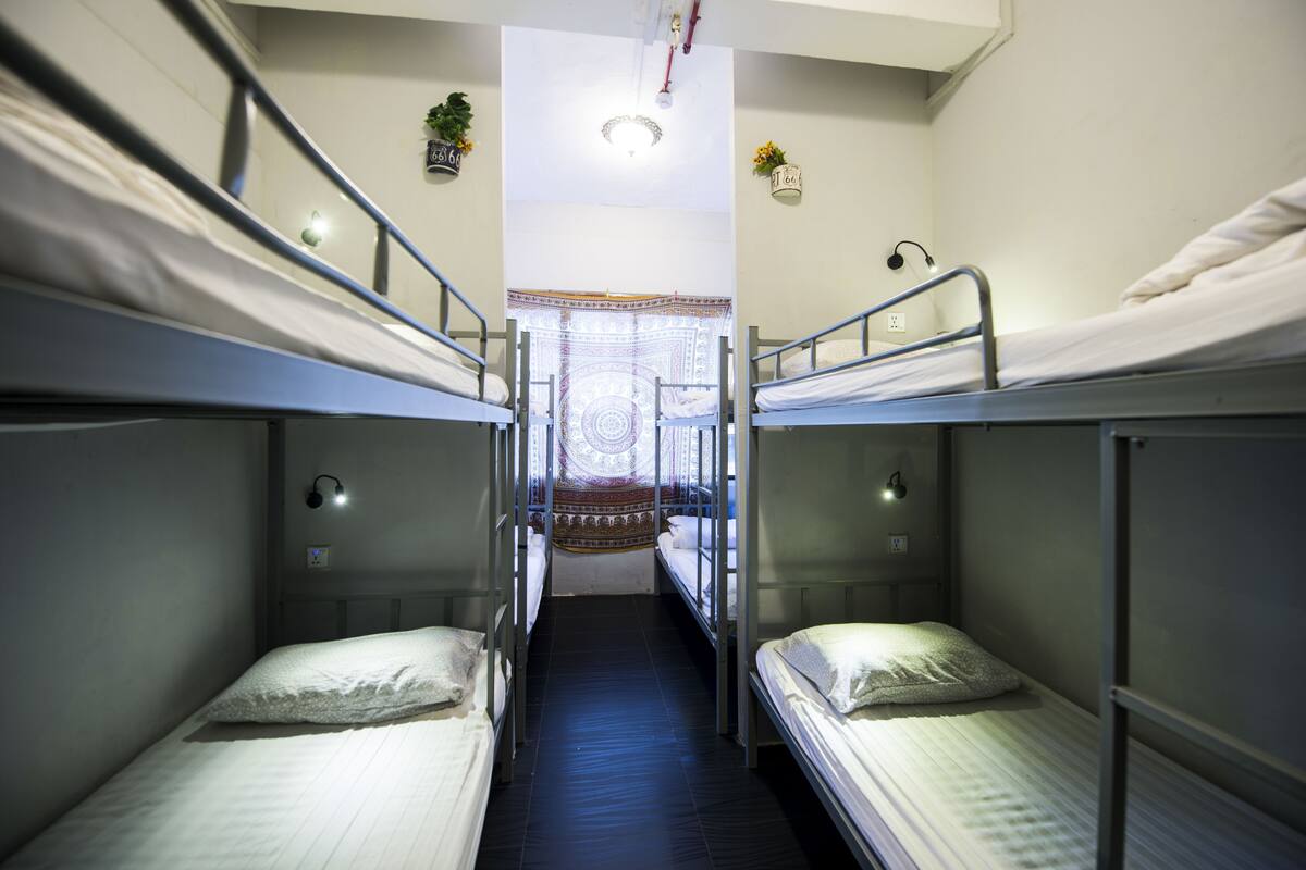 Une chambre de dortoir avec des lits superposés, une petite fenêtre avec un rideau et un luminaire au plafond.