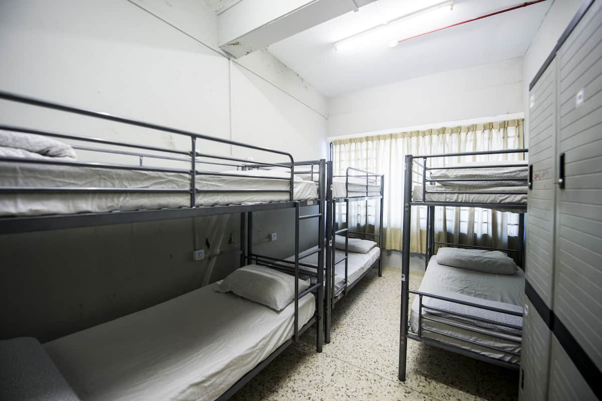 Une chambre de dortoir avec des lits superposés, une fenêtre avec des rideaux et un sol carrelé.