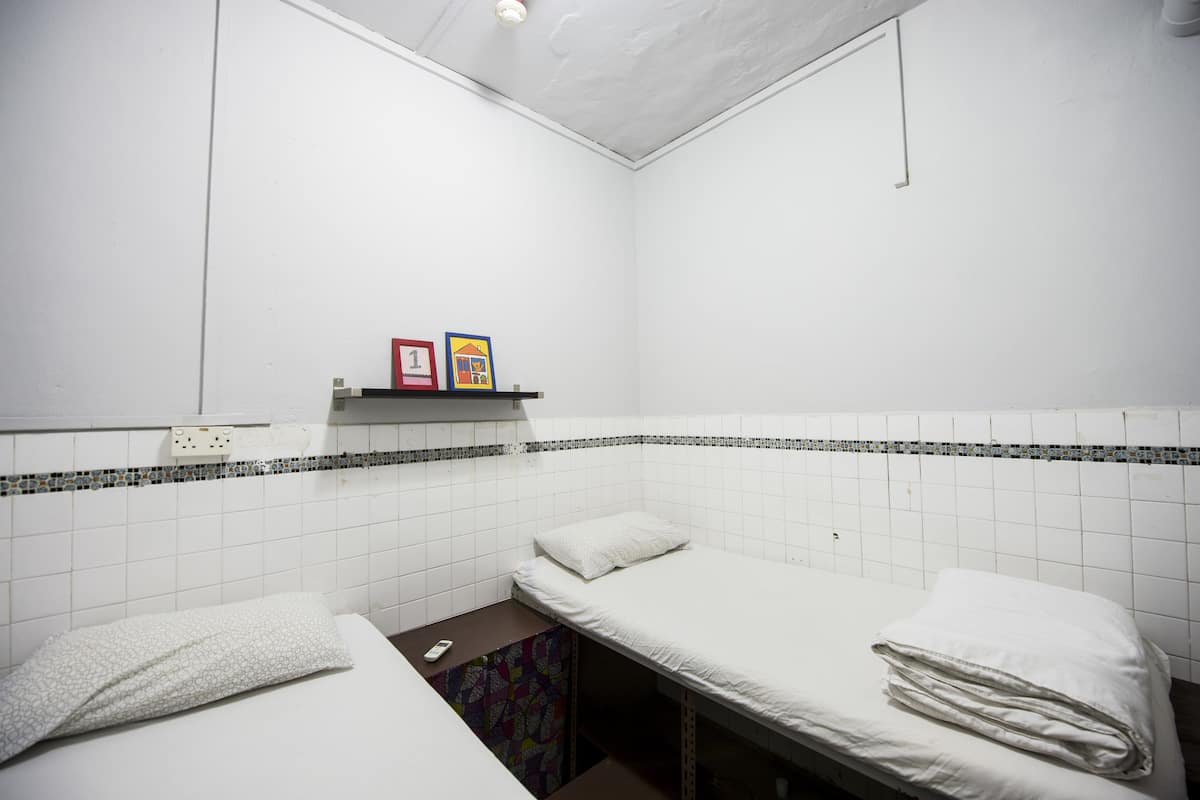 Une petite pièce propre, avec deux lits, une étagère contenant quelques objets et un mur recouvert de carreaux.