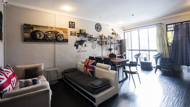 A modern living room with a sofa, a dining table, and a kitchen area visible through an open door. - Urban Hostel (Singapore)